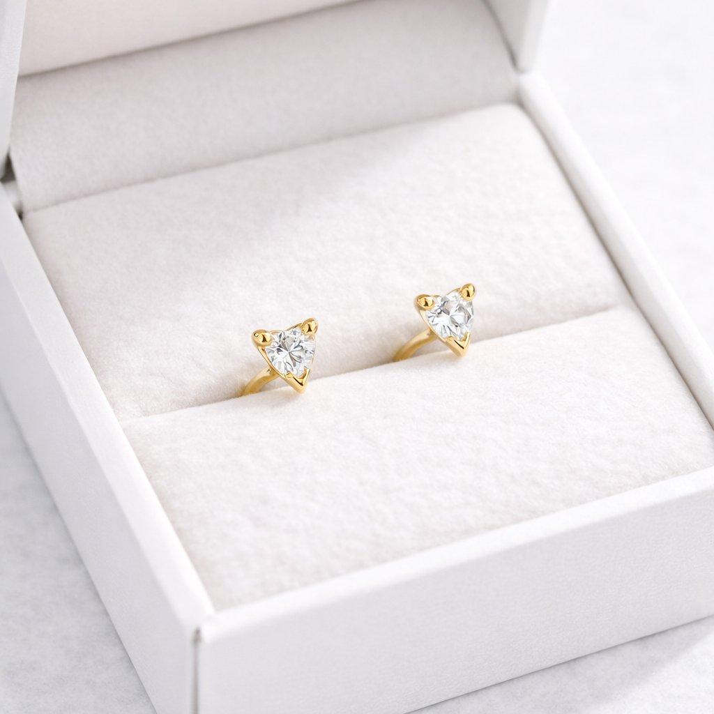 Gold stud earrings in a white jewelry box on a light gray background